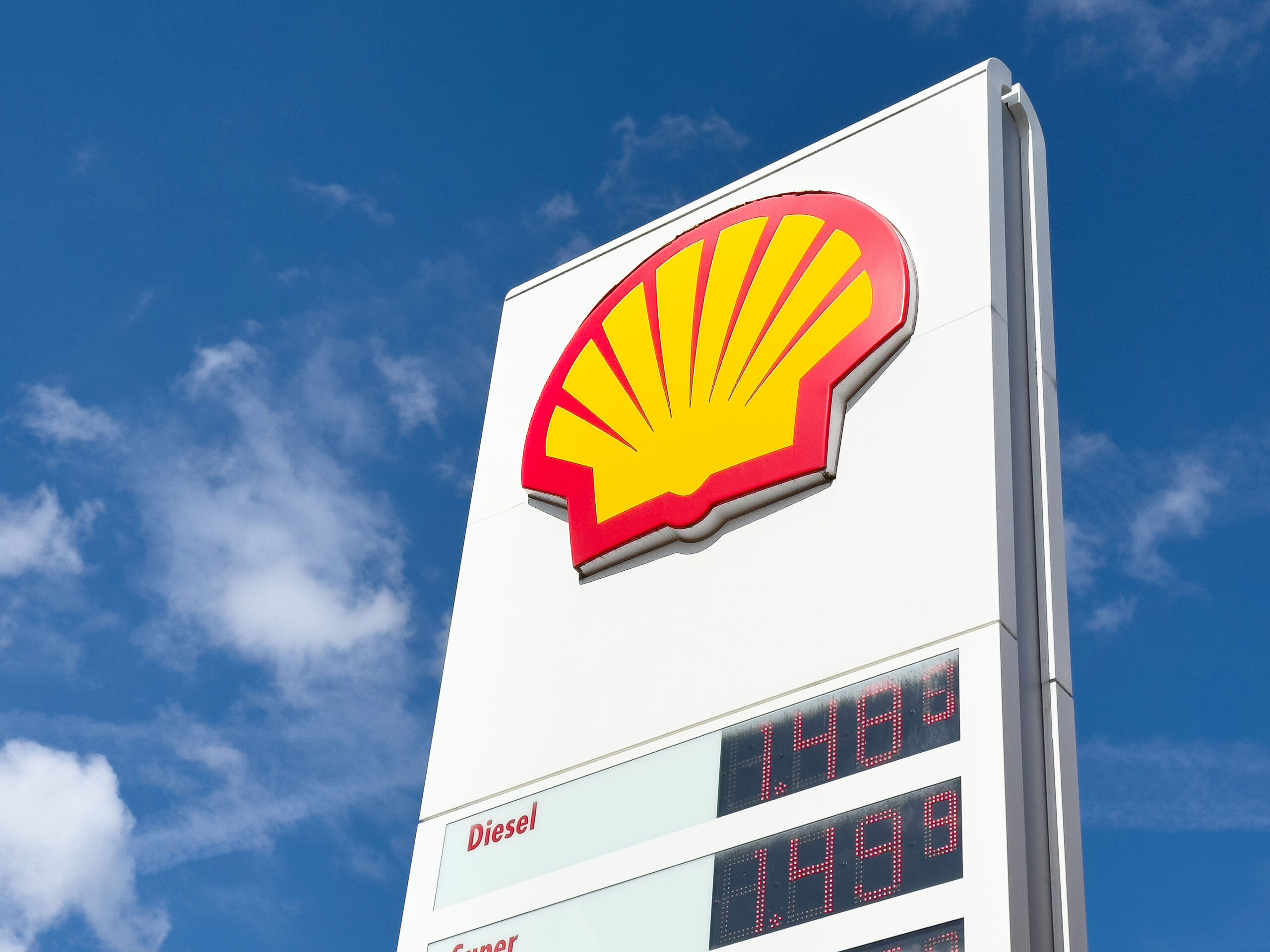 Shell gas station sign with fuel prices displayed against blue sky